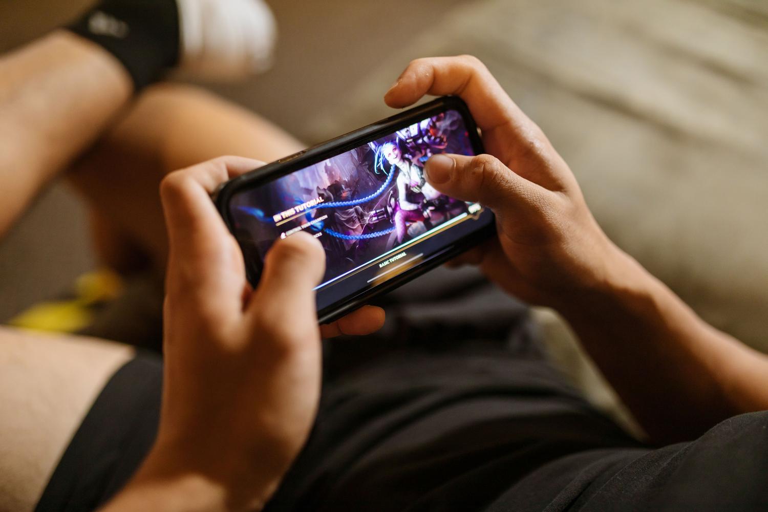 Primer plano de manos utilizando un dispositivo móvil para jugar, destacando la interfaz táctil en el gaming Android.