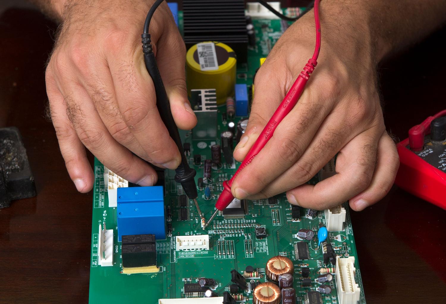 Primer plano de manos expertas utilizando sondas de un medidor de voltaje sobre una placa de circuito impreso, ilustrando la precisión en la electrónica DIY.