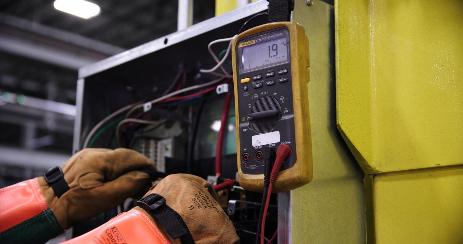 Electricista profesional utilizando un multímetro digital para medir la tensión en un panel de control industrial, enfatizando la seguridad y el equipo de protección.