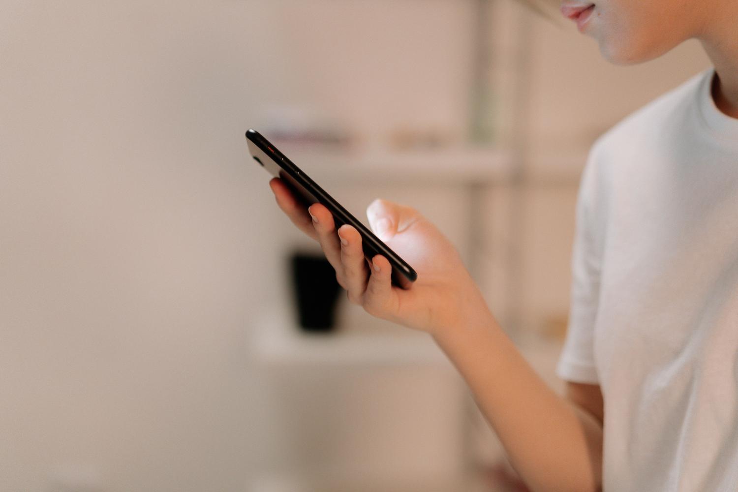 Primer plano de una mano utilizando un iPhone en un entorno interior, enfocándose en la manipulación del dispositivo.