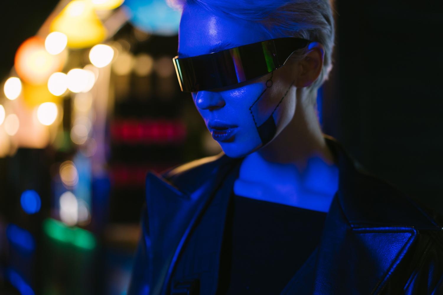 Retrato de una mujer con gafas tecnológicas futuristas bajo luces de neón, representando la identidad digital y los avatares.